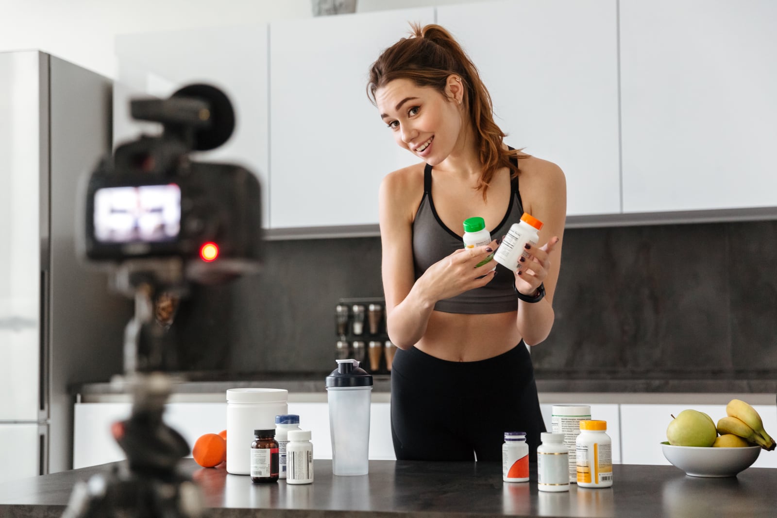 Creadora grabando un video de producto en casa, sosteniendo frascos de suplementos